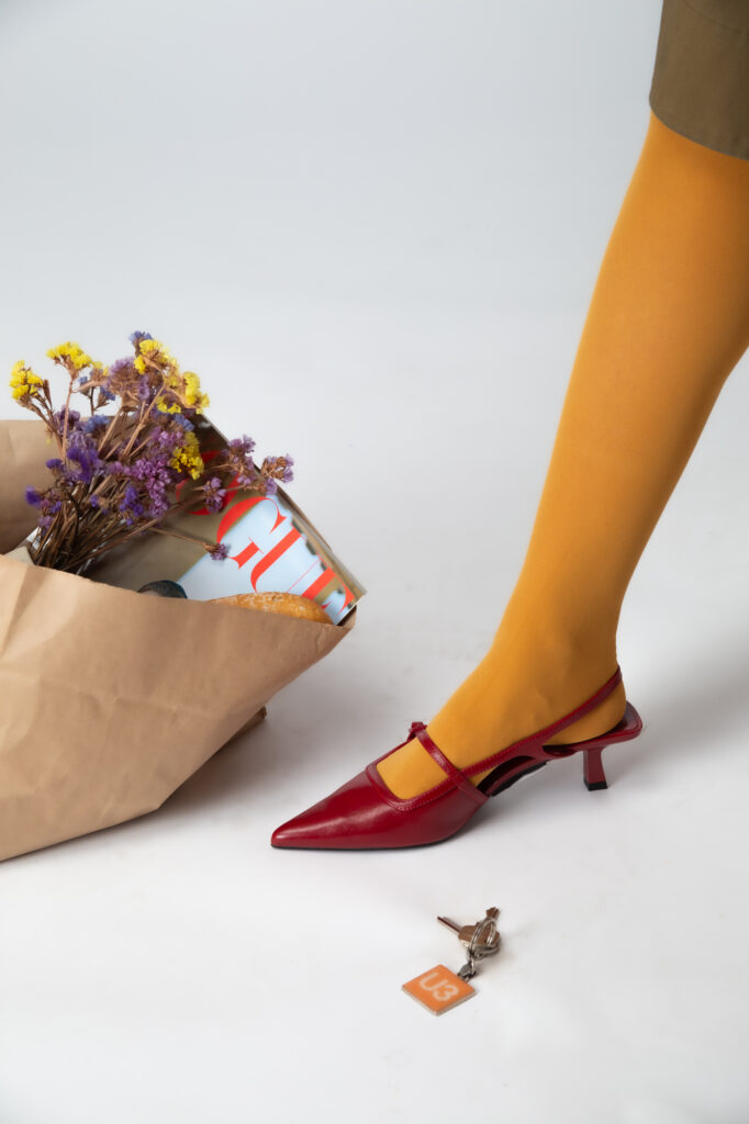 Commercial fashion photography by Łukasz Zając, detail of yellow tights and red shoes with a paper bag of flowers, Kraków, Poland