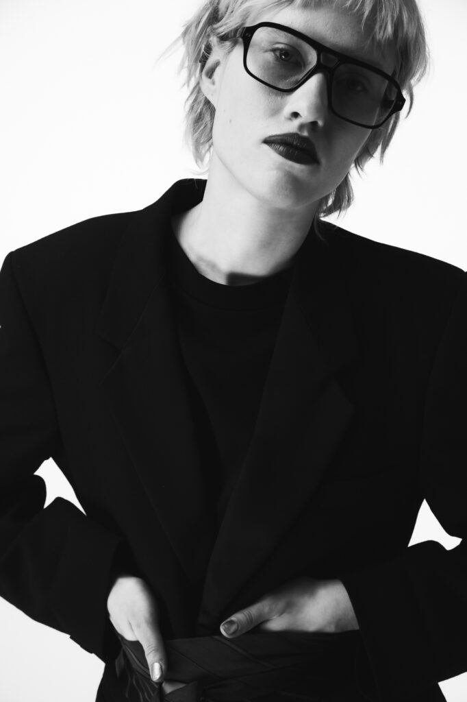 Editorial portrait photography by Łukasz Zając, fashion-forward portrait of a person in a sharp black suit and sunglasses, Krakow, Poland