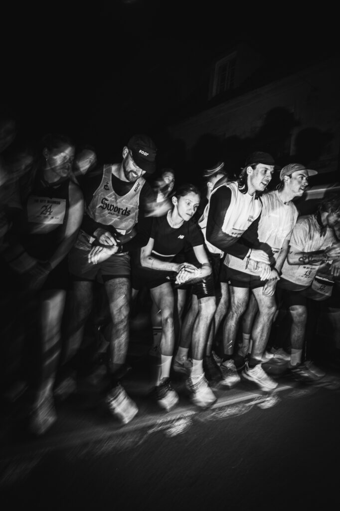 Street and lifestyle photography by Łukasz Zając, black and white wide shot of a group of people standing together at night, Kraków, Poland