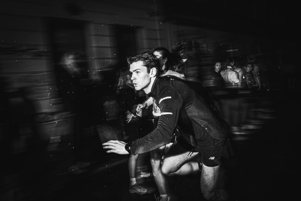 Sports and running photography by Łukasz Zając, black and white motion-blurred action shot of runners during a night event, Kraków, Poland