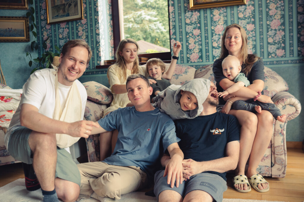 Lifestyle photography by Łukasz Zając, large family group posing together on a couch in a cozy room with patterned wallpaper, Kraków, Poland