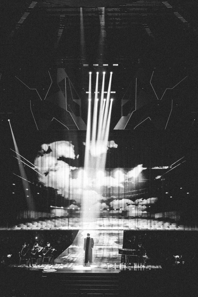 Culture and events stage and concert photography by Łukasz Zając, wide dramatic view of a stage with vertical spotlights and performer, Kraków, Poland
