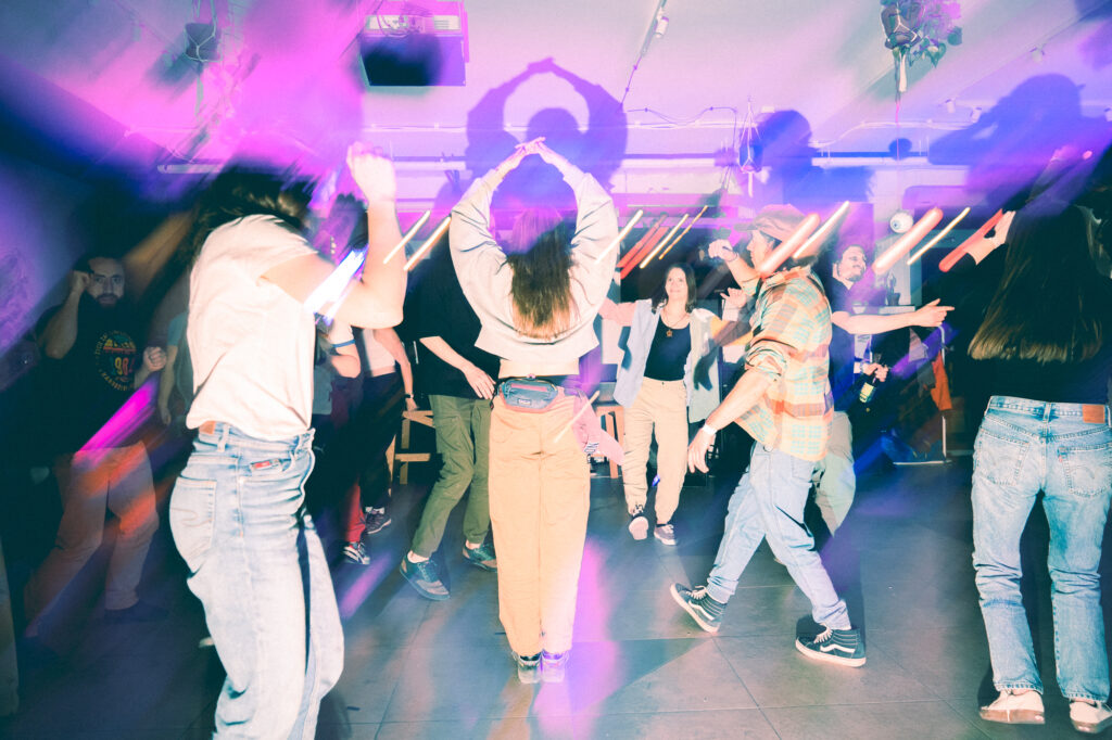 Lifestyle photography by Łukasz Zając, group of people dancing together on a crowded dance floor under atmospheric purple lighting, Kraków, Poland