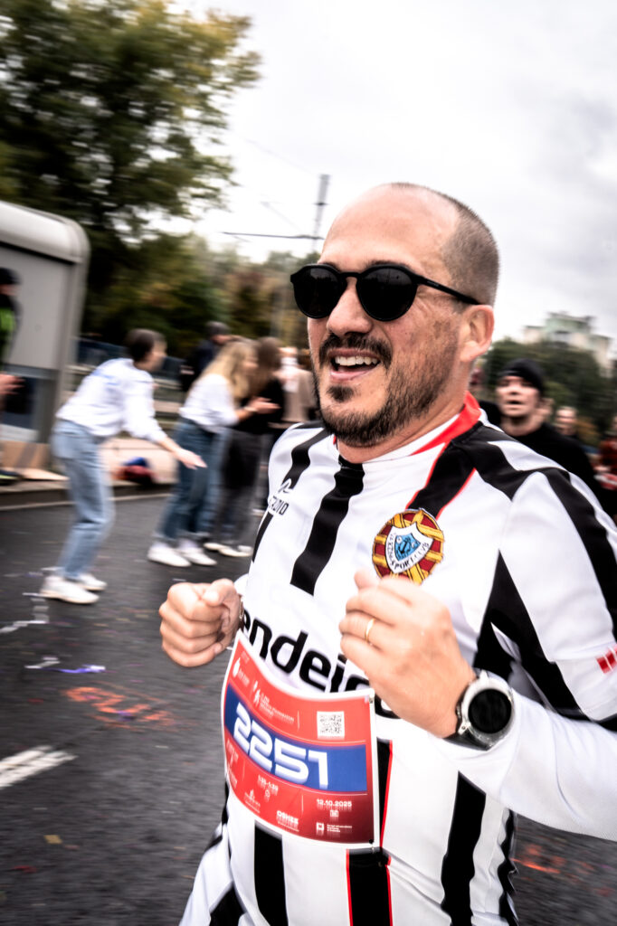 Sports portrait photography by Łukasz Zając, smiling runner wearing sunglasses and a striped athletic jersey at a race event, Poland