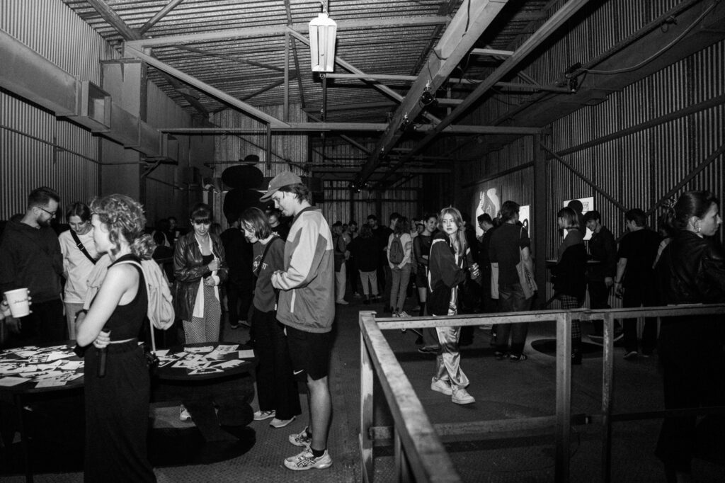 Art and gallery photography by Łukasz Zając, black and white wide shot of people gathering and socializing inside an industrial exhibition space, Kraków, Poland