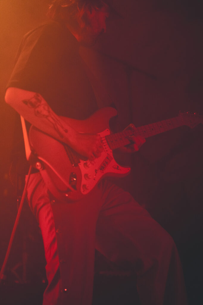 Culture and events concert photography by Łukasz Zając, guitarist performing under dramatic red stage lights, Kraków, Poland