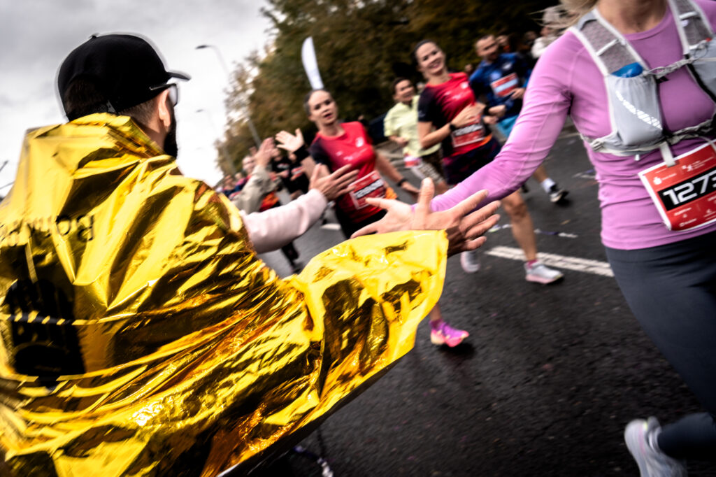 Sports and event photography by Łukasz Zając, participants high-fiving during a running event with one person wrapped in a gold thermal foil blanket, Kraków, Poland
