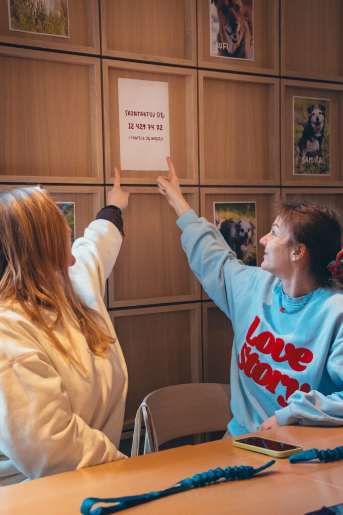 Lifestyle and social event photography, capturing Two people hanging posters or notices on a wooden wall panel by Łukasz Zając in Cracow, Poland.