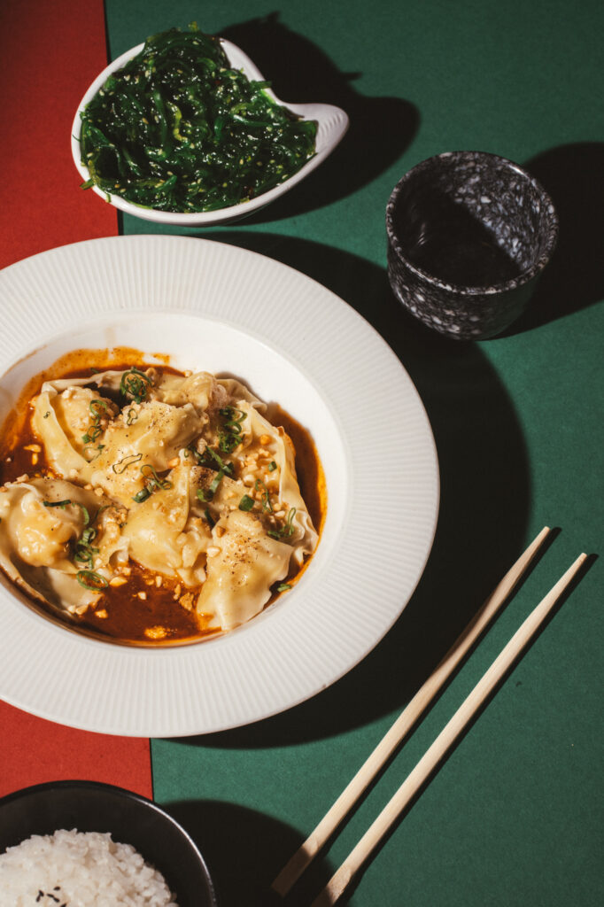 Commercial food photography by Łukasz Zając, dumplings in a white plate with chopsticks on a green and red background, Kraków, Poland