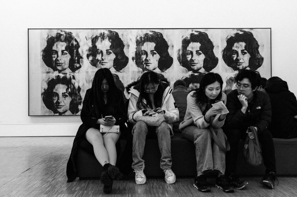 Art and culture photography by Łukasz Zając, visitors sitting and looking at contemporary multi-panel portraits displayed in a gallery, Kraków, Poland