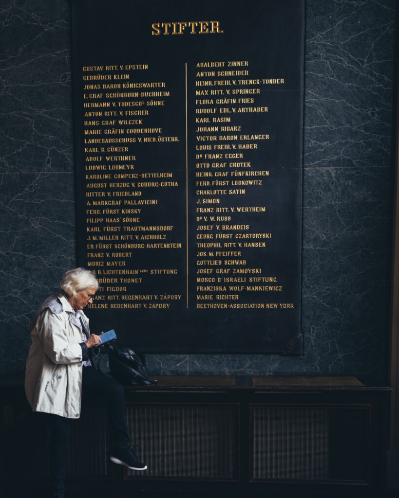 Art and culture photography by Łukasz Zając, person standing next to a large dark wall with inscribed donor names or text, Kraków, Poland