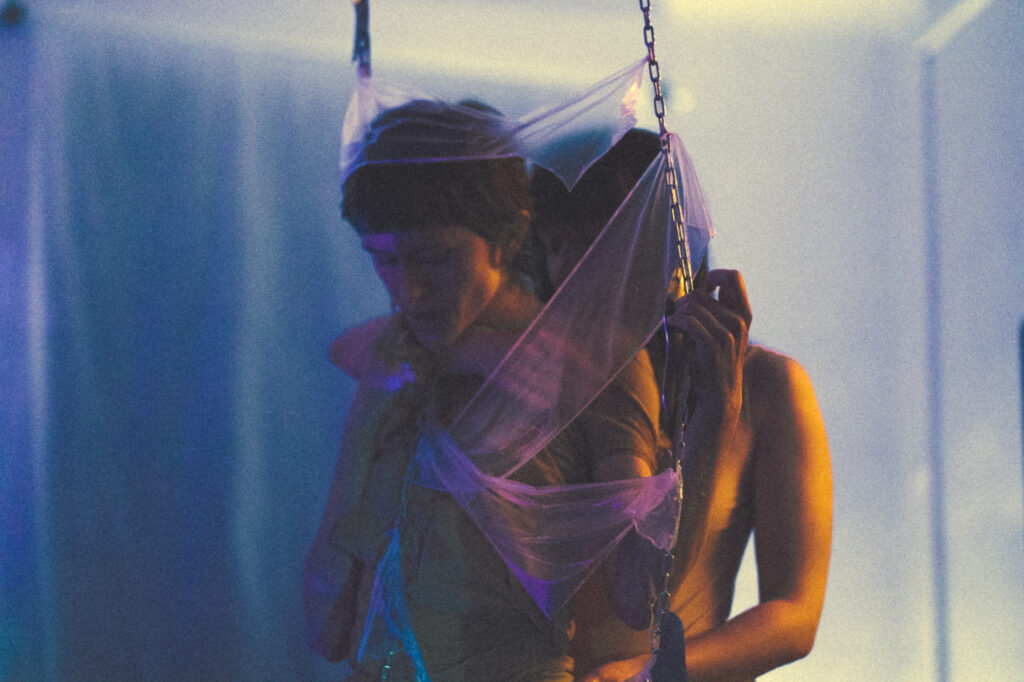 Contemporary art and installation photography by Łukasz Zając, artistic shot of a person surrounded by abstract hanging materials with moody lighting, Kraków, Poland