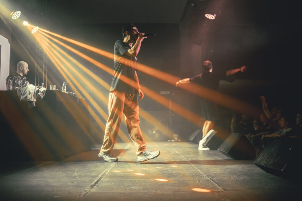 Culture and events concert photography by Łukasz Zając, performer on stage with striking diagonal golden beams of light and spotlight effects, Poland