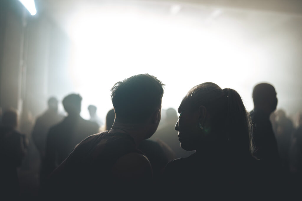 Culture and events concert photography by Łukasz Zając, silhouettes of audience members facing each other in a dimly lit venue, Poland