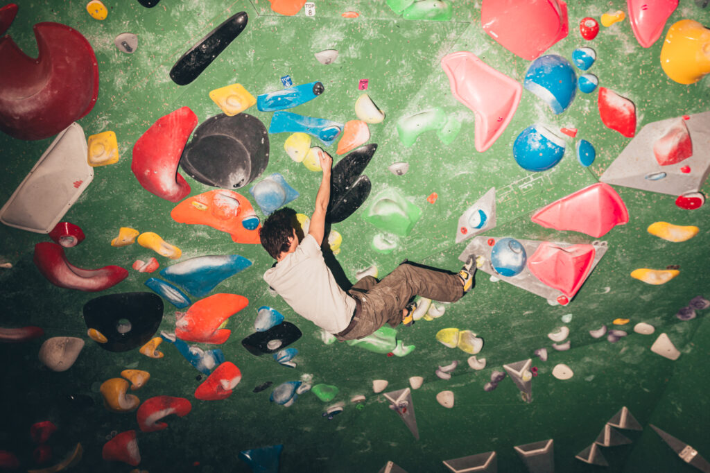 Sports photography by Łukasz Zając, high-angle wide view of a climber navigating colorful holds on a boulder wall, Poland