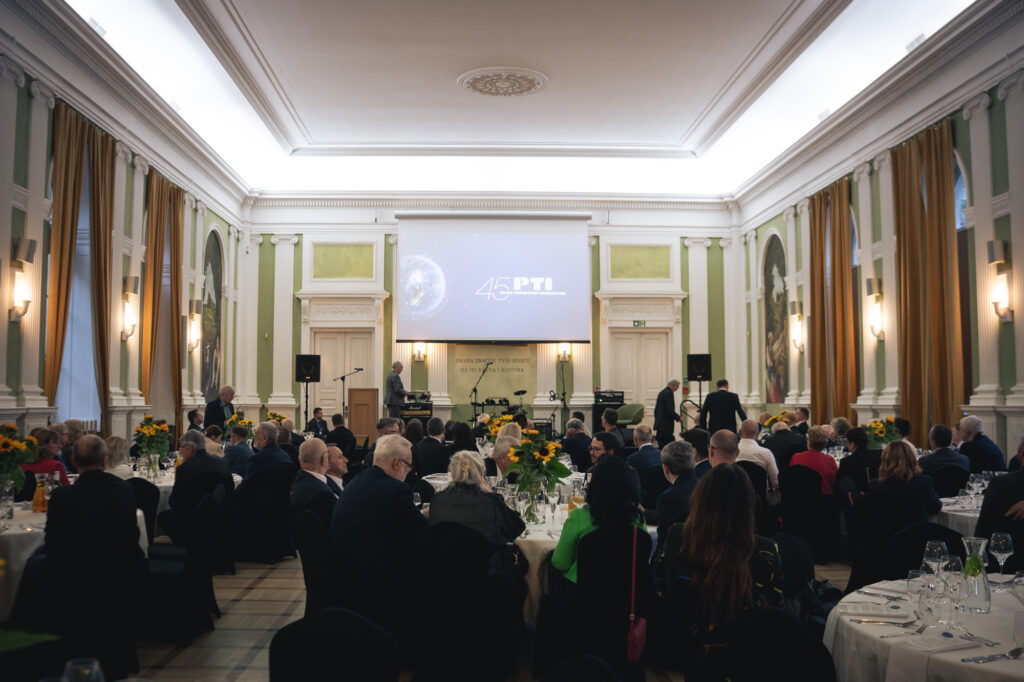 A wide shot of an elegant, large conference hall filled with seated attendees facing a stage.