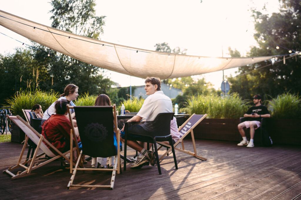 Lifestyle and event photography by Łukasz Zając, outdoor gathering of people relaxing on a wooden deck under a canopy during late afternoon, Kraków, Poland