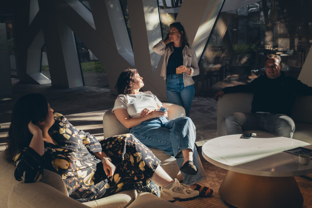A group of people relaxing and socializing together in a modern, sunlit lounge area with contemporary furniture.