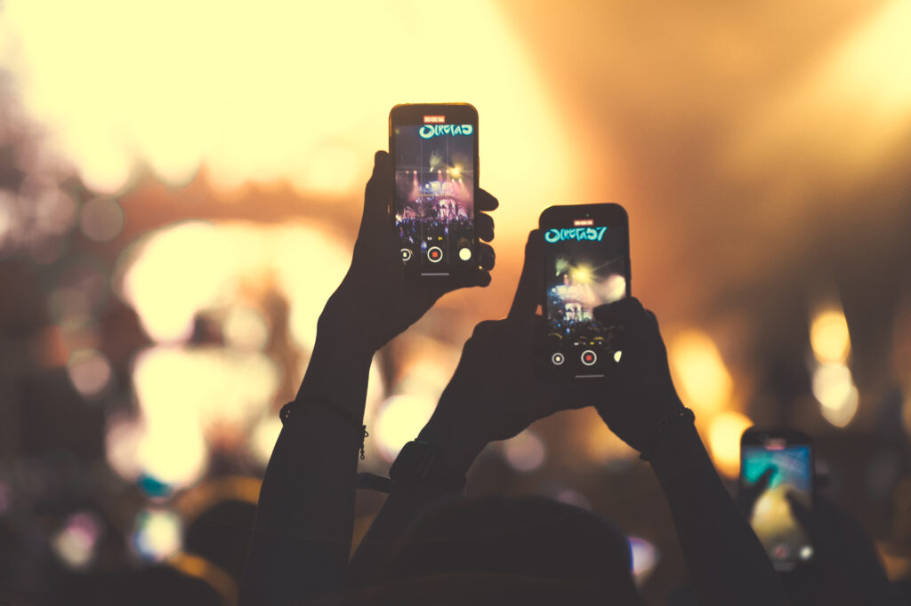 Culture and events concert photography by Łukasz Zając, silhouettes of audience members holding up phones to record a concert, Kraków, Poland