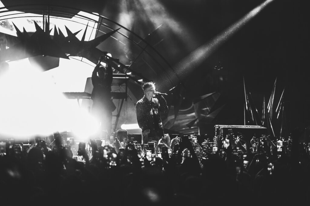 Culture and events concert photography by Łukasz Zając, wide shot of an artist performing on a stage with dramatic lights and crowd in black and white, Kraków, Poland