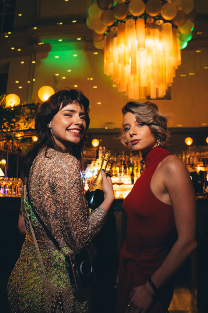 Lifestyle photography by Łukasz Zając, two women smiling together indoors with warm ambient lighting, Kraków, Poland