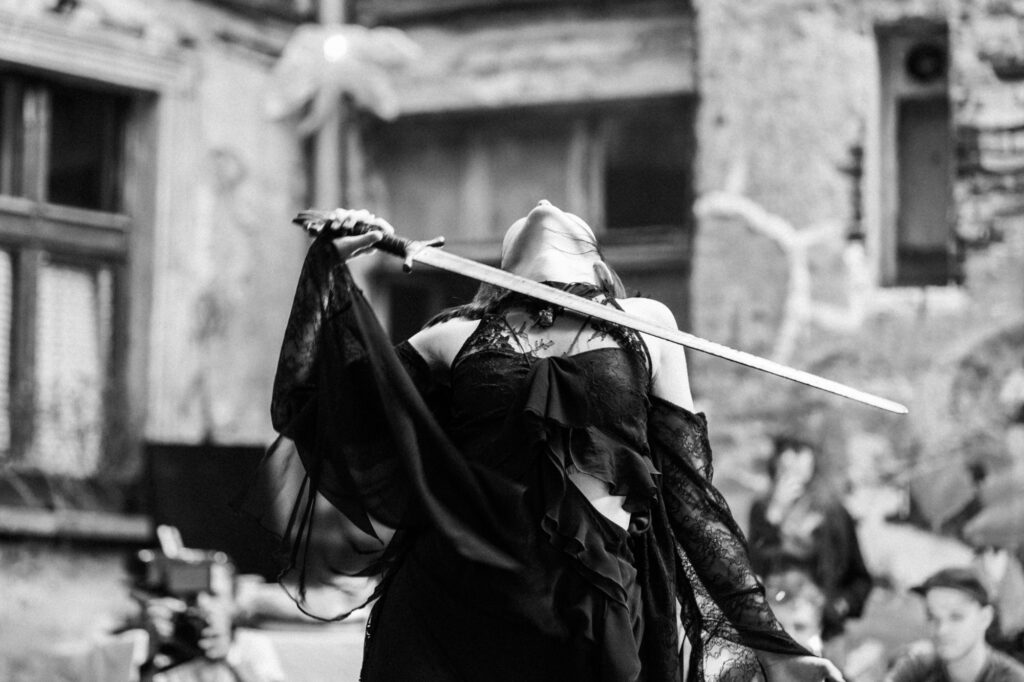Art and performance photography by Łukasz Zając, black and white shot of a performer holding a long staff or tool outdoors, Kraków, Poland