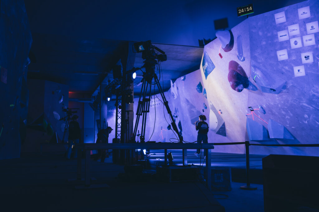 Sports photography by Łukasz Zając, wide nighttime shot of an outdoor climbing wall illuminated by blue stage lights, Kraków, Poland