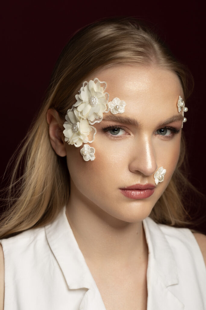 Commercial beauty photography by Łukasz Zając, close-up portrait of model with delicate floral accessories on face and soft studio lighting, Krakow, Poland